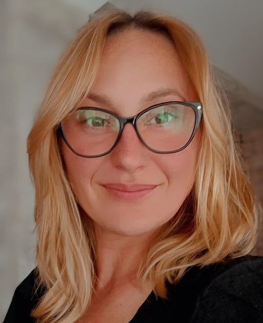 Claudia, creadora del proyecto, sonriente con gafas y cabello rubio en un ambiente acogedor