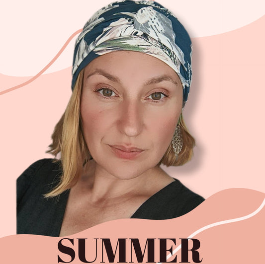Mujer con turbante oncológico verano azul con estampado floral posando con fondo rosa claro