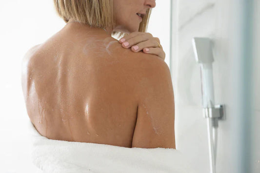 Mujer aplicando productos para piel sensible por quimioterapia en su espalda mientras se ducha