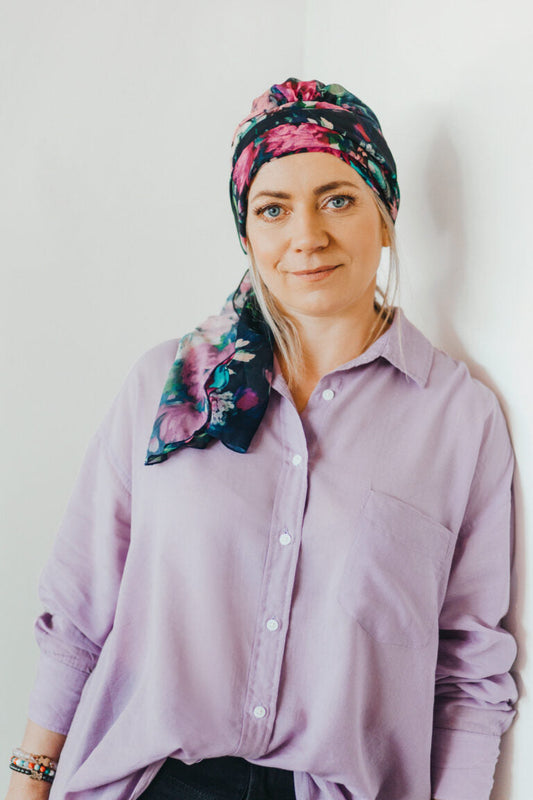 Mujer con turbante floral de colores oscuros apoyada en la pared ejemplo para elegir turbante cáncer