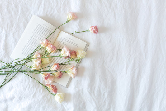 Libro abierto sobre cama blanca con flores rosadas apoyadas simbolizando el cuidado de las secuelas psicológicas del cáncer