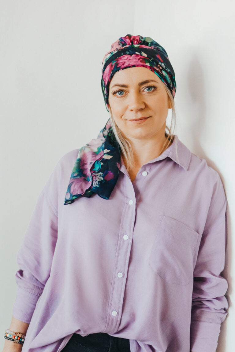 Mujer con turbante floral de colores oscuros apoyada en la pared ejemplo para elegir turbante cáncer