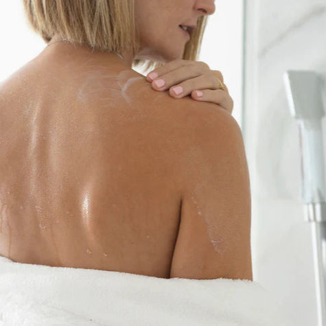 Mujer aplicando aceite de ducha suave de GGCare en la piel durante el baño